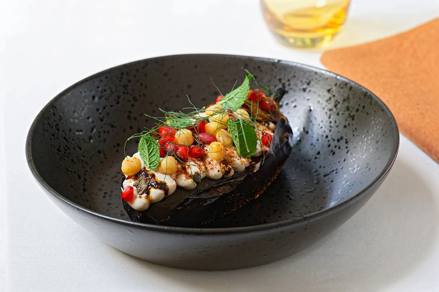 Geröstete Aubergine in einer schwarzen Bowl gefüllt mir Kichererbsen und Granatapfelkernen