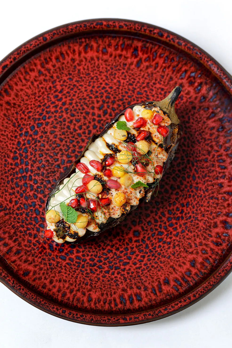 Geröstete Aubergine in einer schwarzen Bowl gefüllt mir Kichererbsen und Granatapfelkernen